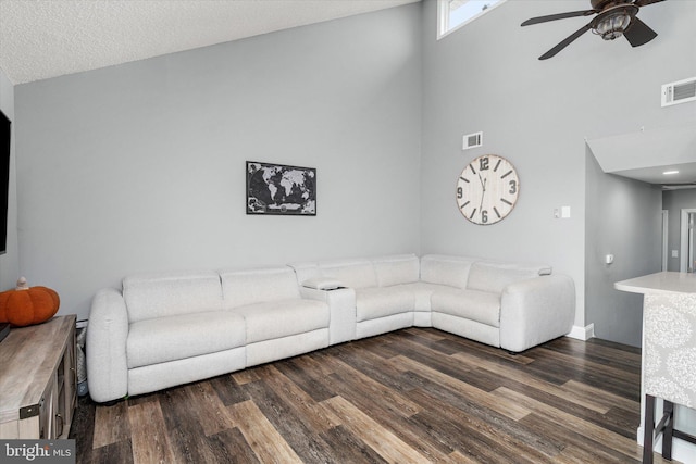 living room with ceiling fan, a textured ceiling, dark hardwood / wood-style flooring, and a towering ceiling