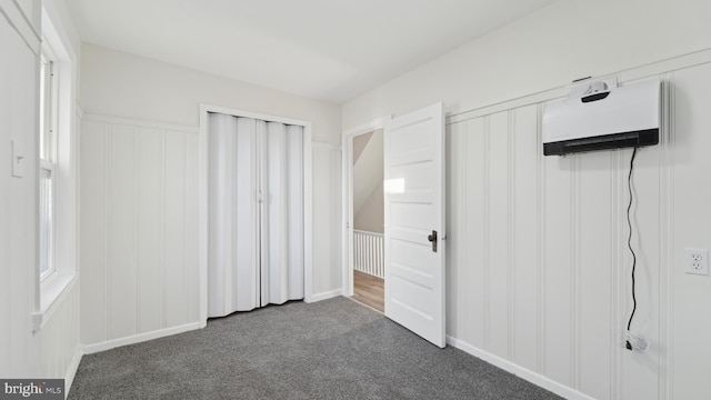 unfurnished bedroom featuring a wall mounted air conditioner, a closet, and dark colored carpet