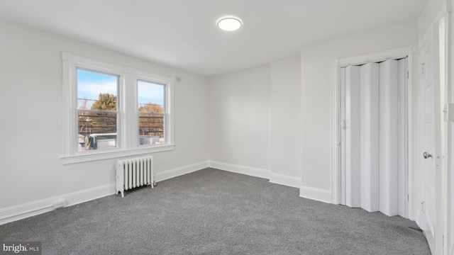 spare room with radiator heating unit and dark colored carpet