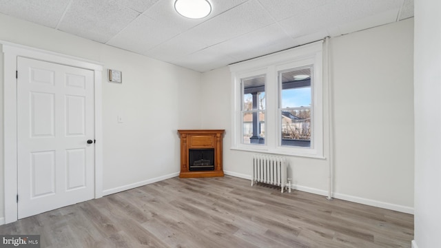 spare room with radiator, a drop ceiling, and light hardwood / wood-style floors