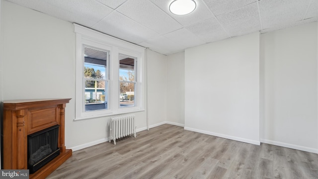 unfurnished living room featuring a drop ceiling, radiator, and light hardwood / wood-style floors