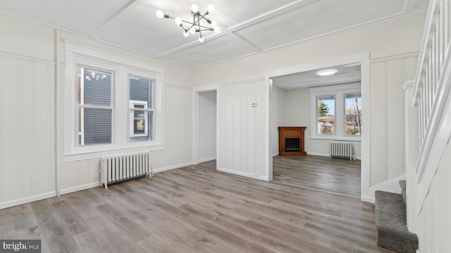 unfurnished living room with a notable chandelier, radiator, and light wood-type flooring