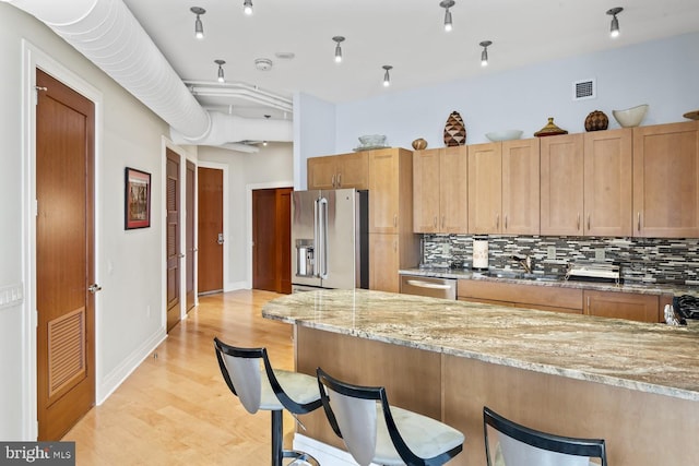 kitchen with light stone countertops, decorative backsplash, stainless steel appliances, and a kitchen breakfast bar