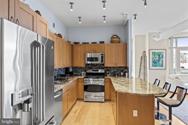 kitchen with appliances with stainless steel finishes, a breakfast bar, light wood-type flooring, and backsplash