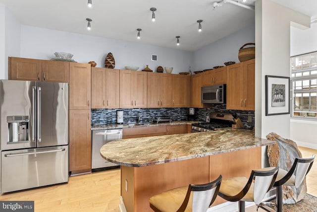 kitchen featuring a breakfast bar, tasteful backsplash, appliances with stainless steel finishes, kitchen peninsula, and light stone countertops