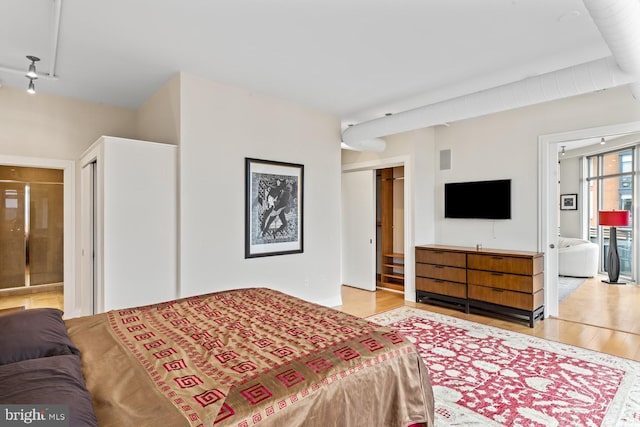 bedroom with rail lighting, ensuite bathroom, and light wood-type flooring