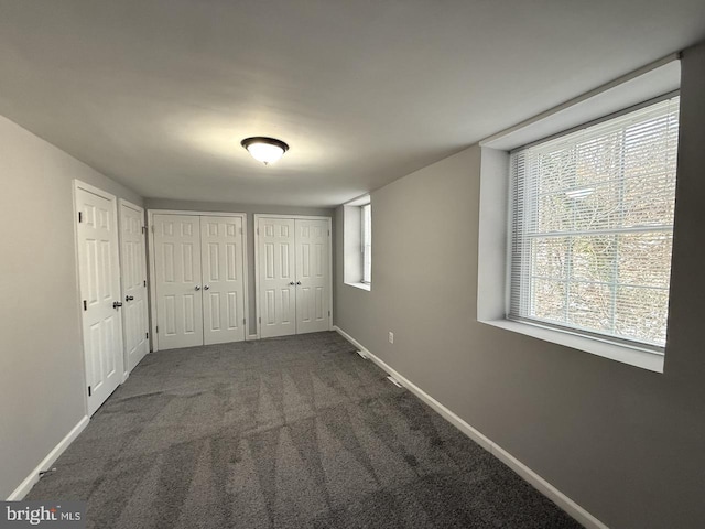 unfurnished bedroom with two closets and dark carpet