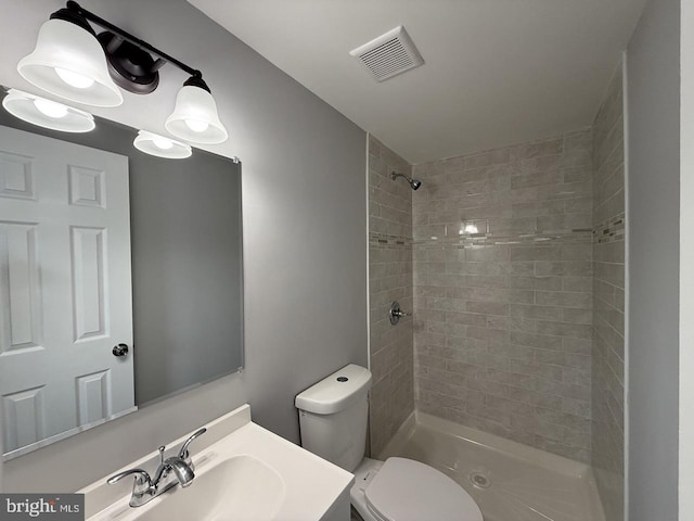 bathroom with a tile shower, toilet, and vanity