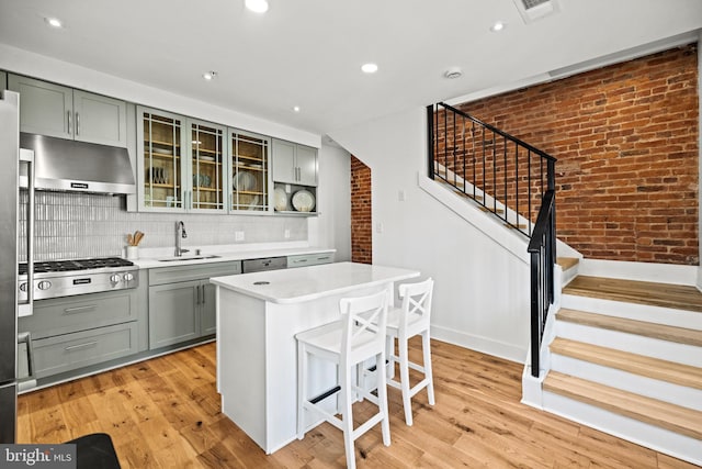 kitchen with brick wall, appliances with stainless steel finishes, a kitchen island, sink, and range hood