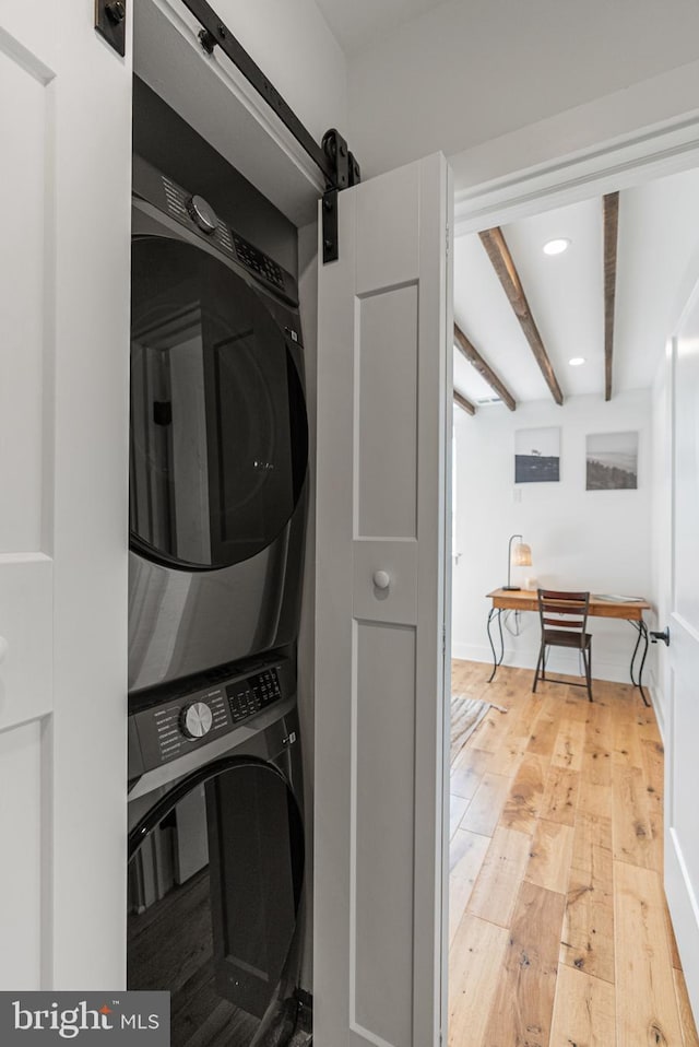 washroom featuring a barn door, stacked washer and clothes dryer, and light hardwood / wood-style floors