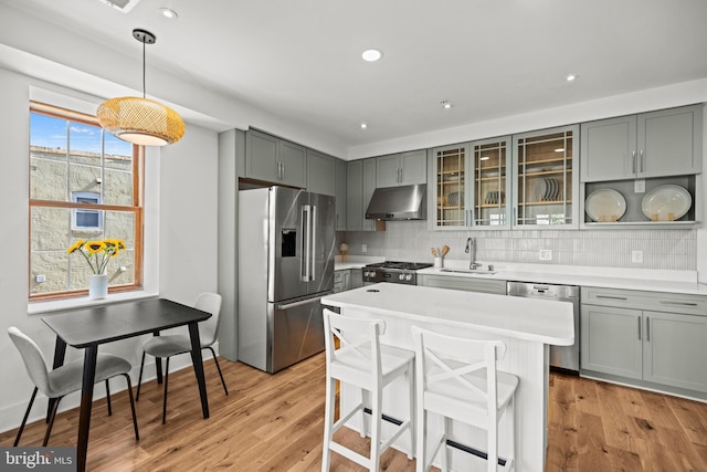 kitchen featuring appliances with stainless steel finishes, backsplash, decorative light fixtures, light wood-type flooring, and sink