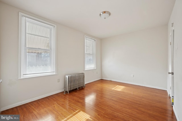 unfurnished room featuring wood-type flooring, radiator, and a healthy amount of sunlight