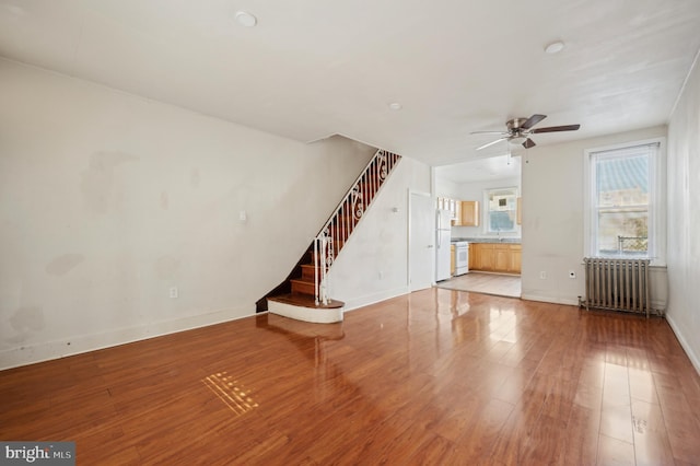 unfurnished living room featuring ceiling fan, hardwood / wood-style floors, and radiator heating unit