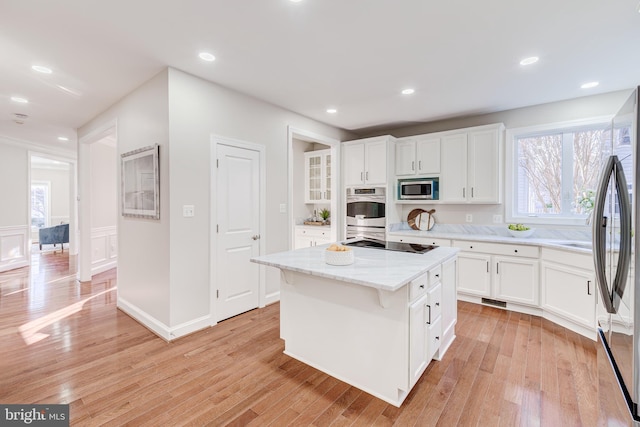 kitchen featuring white cabinetry, stainless steel appliances, a center island, light stone counters, and light hardwood / wood-style floors