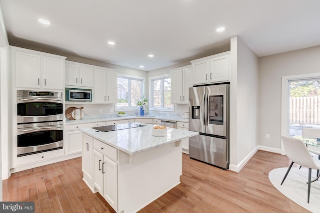 kitchen with a kitchen island, white cabinets, light hardwood / wood-style floors, stainless steel appliances, and light stone countertops