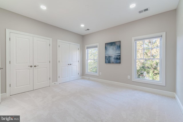 unfurnished bedroom with multiple closets and light colored carpet