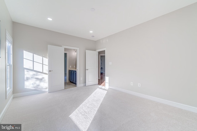 unfurnished bedroom featuring multiple windows, connected bathroom, and light colored carpet