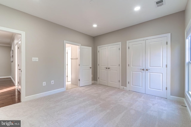 unfurnished bedroom with light colored carpet and two closets