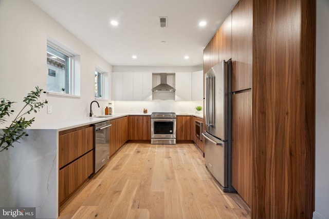 kitchen featuring appliances with stainless steel finishes, wall chimney exhaust hood, sink, white cabinets, and light hardwood / wood-style floors