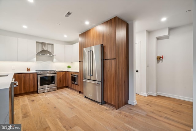 kitchen with wall chimney exhaust hood, light wood-type flooring, white cabinetry, tasteful backsplash, and stainless steel appliances