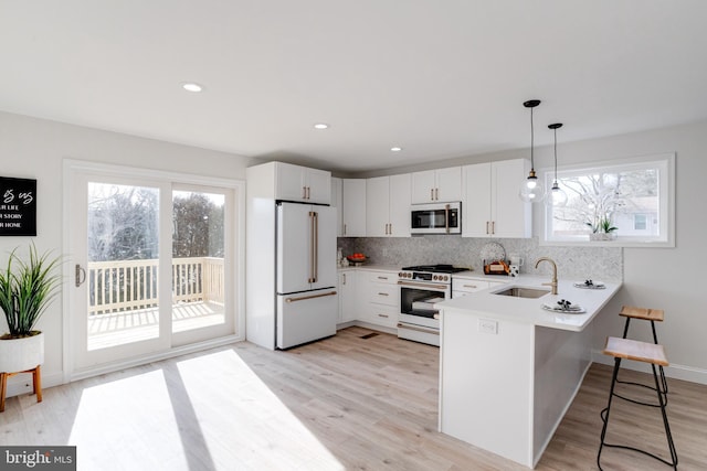 kitchen with sink, high end appliances, hanging light fixtures, kitchen peninsula, and white cabinets