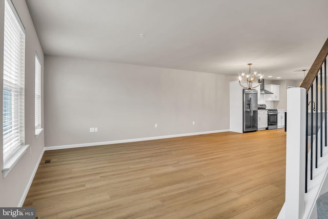 unfurnished living room with light wood-type flooring, a chandelier, and plenty of natural light