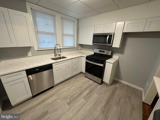 kitchen featuring appliances with stainless steel finishes, a paneled ceiling, white cabinets, light stone counters, and sink