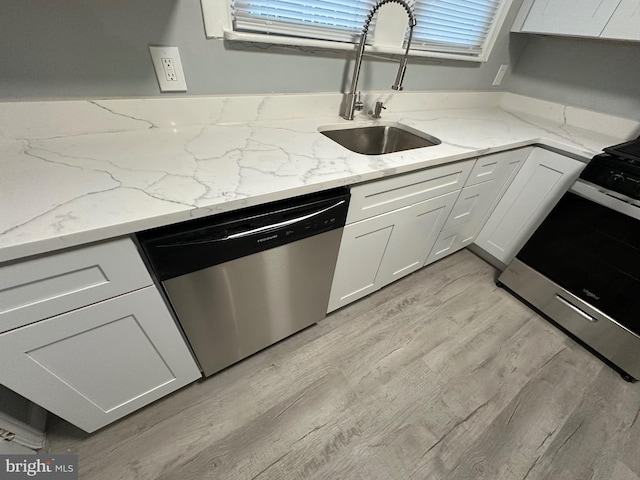 kitchen featuring appliances with stainless steel finishes, light wood-type flooring, white cabinets, light stone counters, and sink