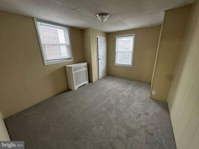 carpeted spare room featuring a drop ceiling and radiator