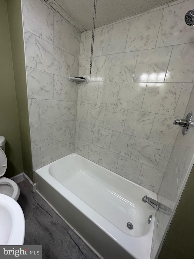 bathroom with wood-type flooring, toilet, and tiled shower / bath combo