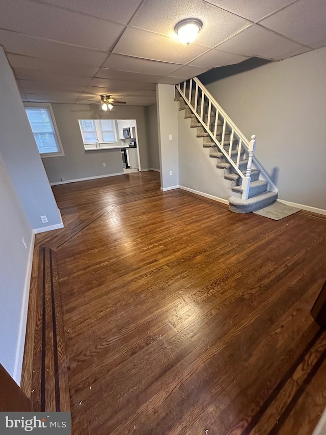 unfurnished living room featuring ceiling fan, a drop ceiling, and dark hardwood / wood-style flooring