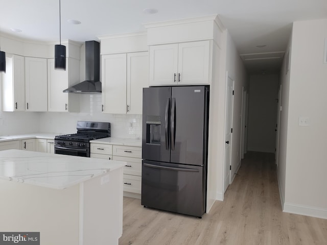 kitchen with gas range oven, wall chimney range hood, black fridge, and light stone countertops