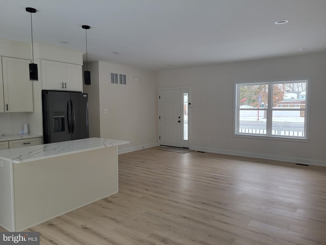 kitchen featuring light stone counters, visible vents, light wood-style flooring, white cabinetry, and black fridge