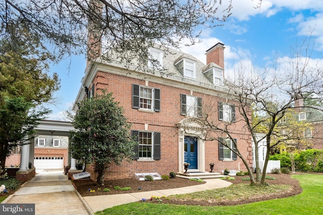 colonial-style house featuring a chimney, brick siding, driveway, and a front lawn