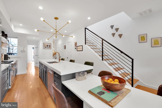 kitchen featuring light hardwood / wood-style floors, pendant lighting, sink, high end stainless steel range oven, and an island with sink