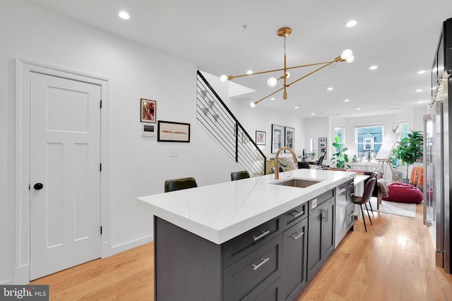 kitchen with pendant lighting, an inviting chandelier, light hardwood / wood-style floors, sink, and a kitchen island with sink