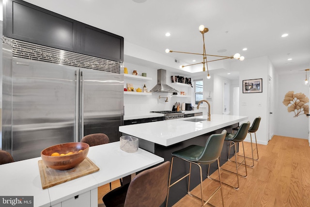 kitchen with ventilation hood, stainless steel appliances, a kitchen island with sink, light wood-type flooring, and sink