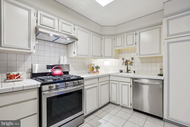 kitchen with light tile patterned flooring, sink, tile counters, stainless steel appliances, and white cabinets