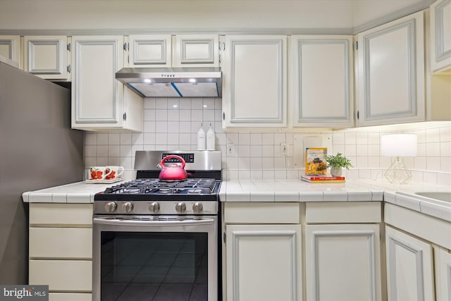 kitchen with tasteful backsplash, tile counters, white cabinets, and appliances with stainless steel finishes