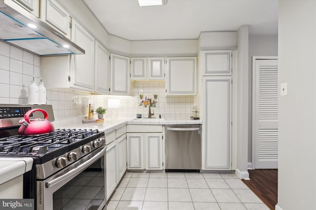 kitchen with light tile patterned flooring, white cabinetry, sink, backsplash, and stainless steel appliances