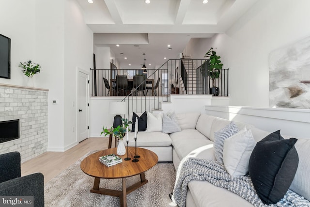 living room with light wood-type flooring, a brick fireplace, and beam ceiling