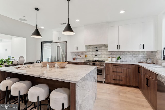 kitchen featuring backsplash, white cabinets, hanging light fixtures, high quality appliances, and light stone counters