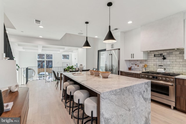 kitchen featuring a kitchen island, coffered ceiling, high end appliances, white cabinetry, and light stone counters