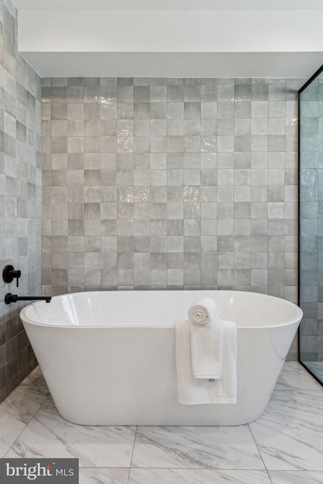 bathroom with a tub to relax in and tile walls