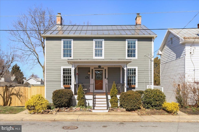 view of front facade with fence, a porch, metal roof, a chimney, and a standing seam roof