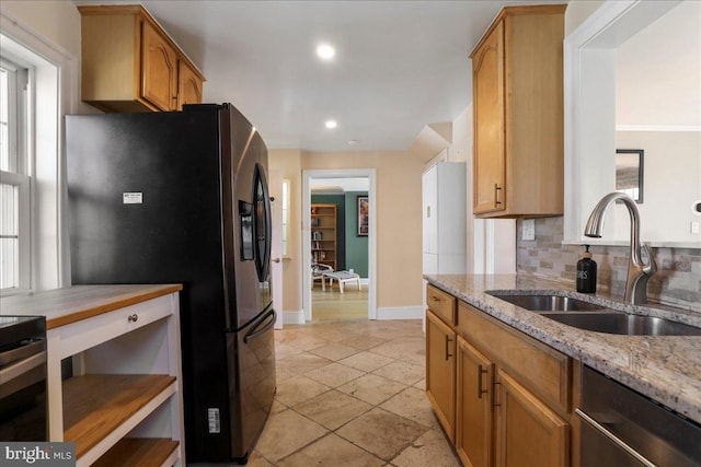 kitchen featuring tasteful backsplash, baseboards, light stone countertops, refrigerator with ice dispenser, and a sink