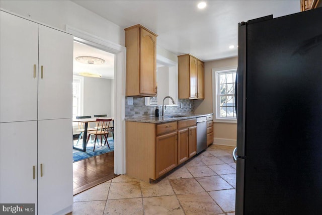 kitchen with a sink, light stone counters, appliances with stainless steel finishes, decorative backsplash, and baseboards