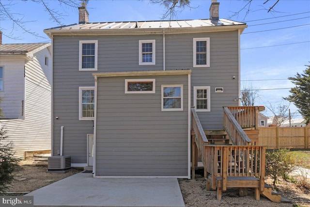 back of house featuring a patio, fence, a chimney, and a standing seam roof