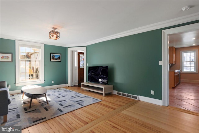 unfurnished living room featuring hardwood / wood-style floors, crown molding, baseboards, and visible vents