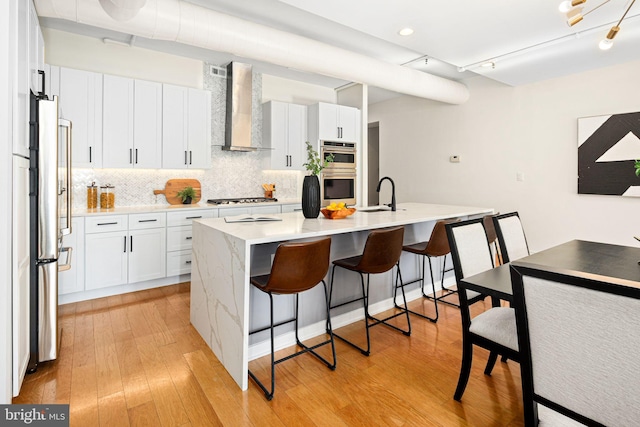 kitchen with white cabinets, an island with sink, wall chimney exhaust hood, and a breakfast bar